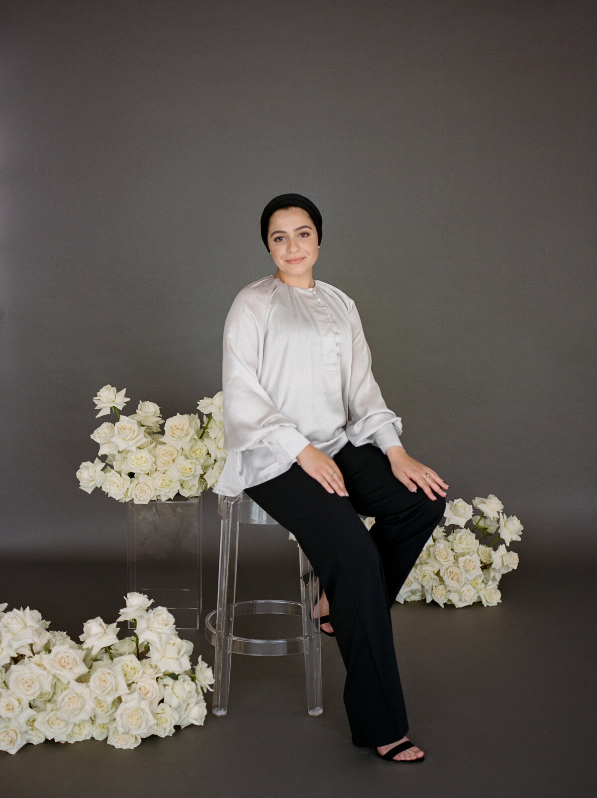 woman in head wrap sits on stool among abundant white roses, dark background, florist branding