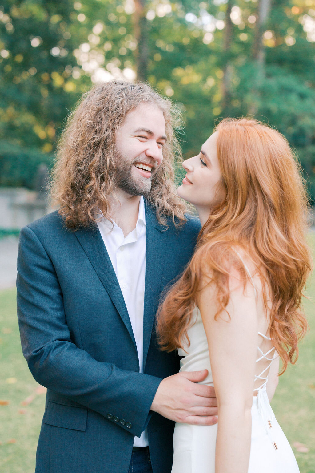 Guy in blue blazer laughs at red head bride on the back lawn of their swan house engagement in atlanta georgia
