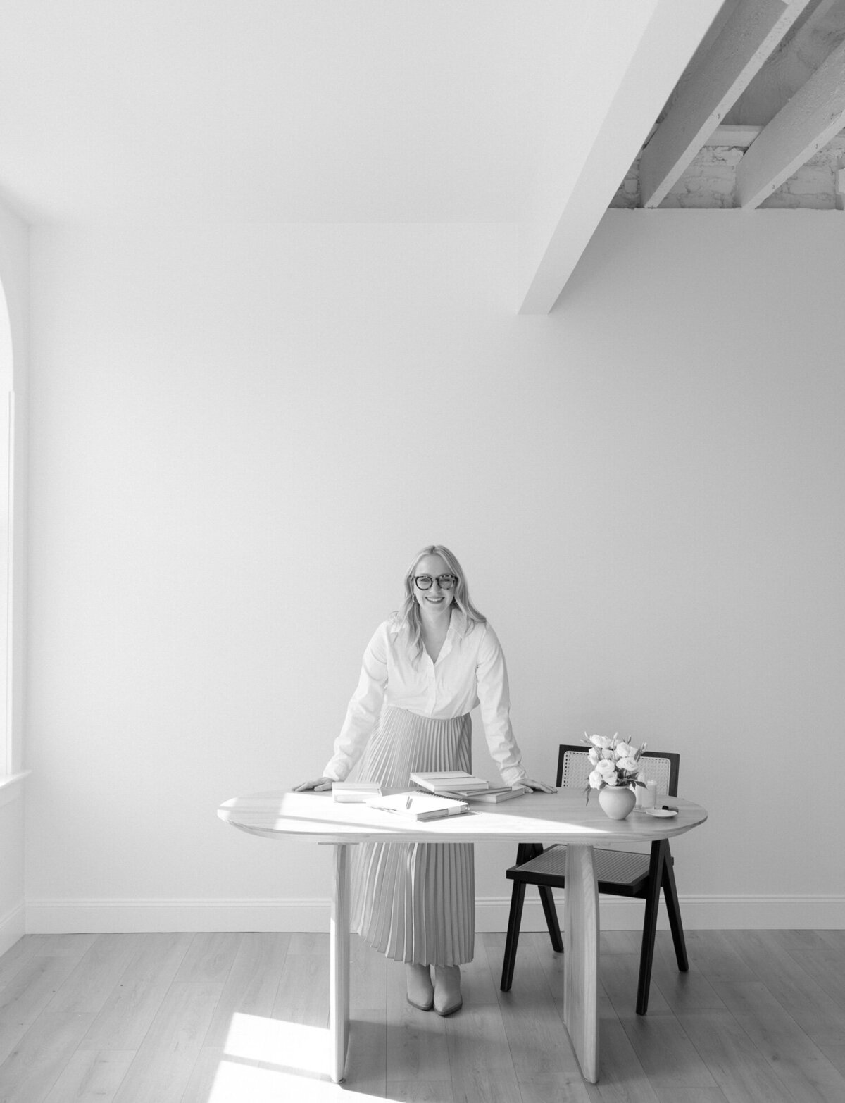 blonde woman in pleated skirt leans on desk during film branding photoshoot