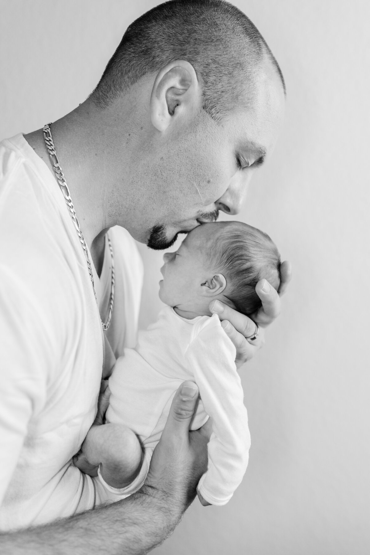 Dad holding newborn baby and kissing forehead in black and white photo in family home