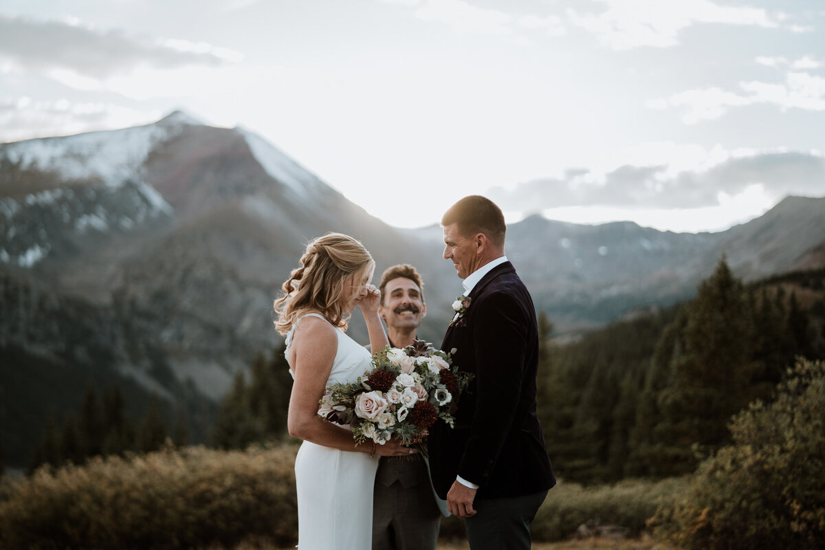 Bride wipes tears while groom smiles during mountain wedding ceremony near Breckenridge, Colorado.