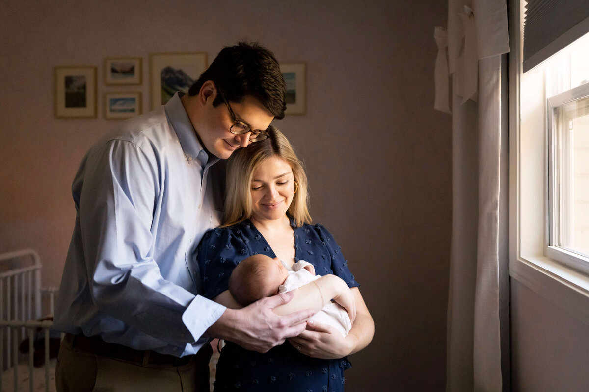 Parents holding newborn daughter while standing next to window