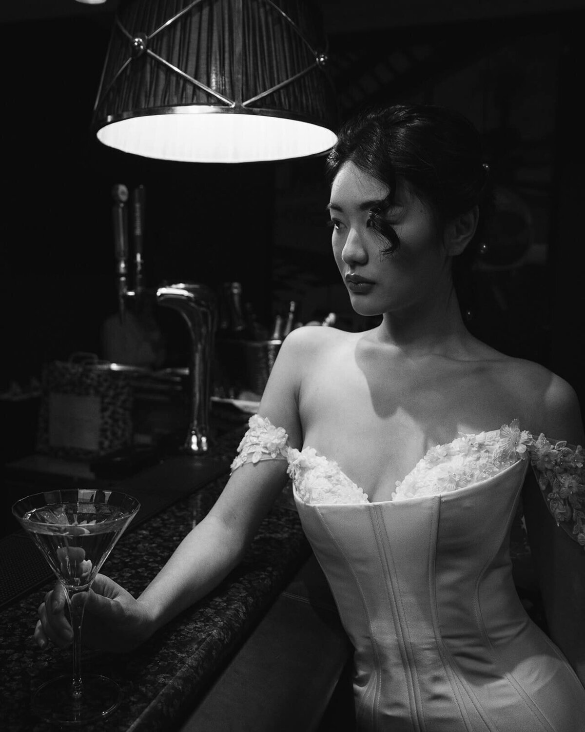a bride holds a cocktail on the bar as she leans into the bar in her vintage wedding dress.