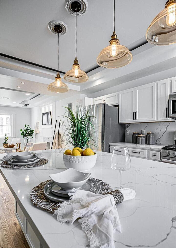 Modern kitchen remodel featuring a quartz waterfall island, custom white cabinetry, stainless steel appliances, and designer pendant lighting—crafted for both elegance and everyday living.