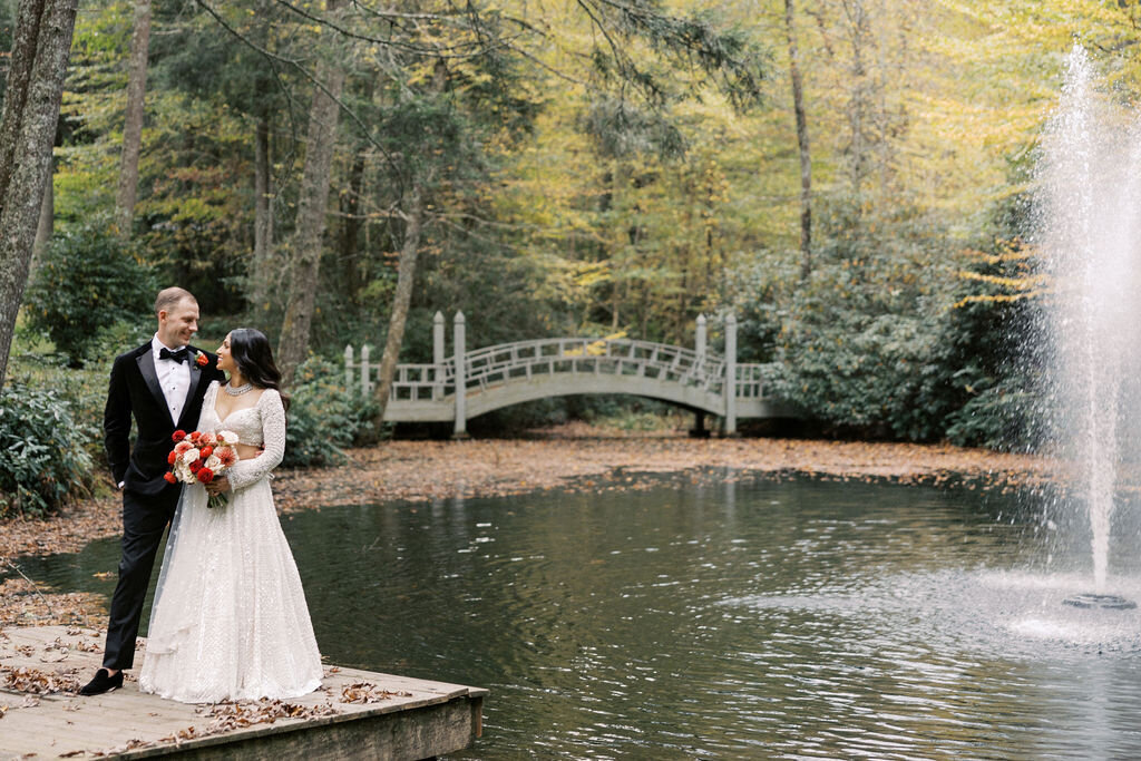 Bride and groom standing on a dock overlooking a pond and water fountain at Old Edwards Inn in Highlands, North Carolina.