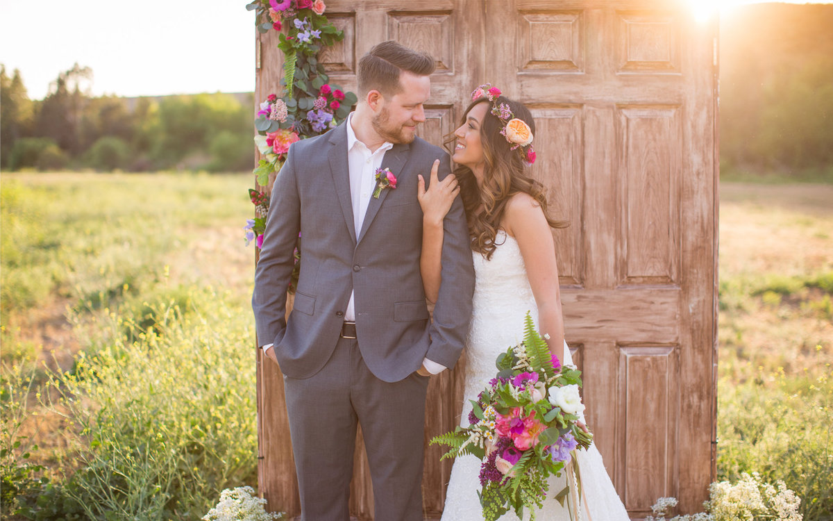 Bride and Groom look to each other during a photo shoot in an open field with a door set up as a prop