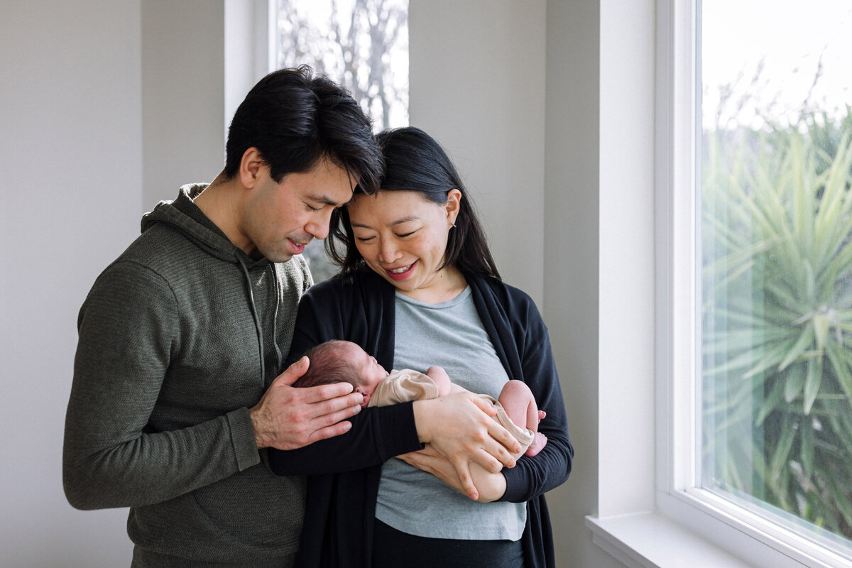 mom holding and smiling at baby while dad holds baby's head and looks down at baby