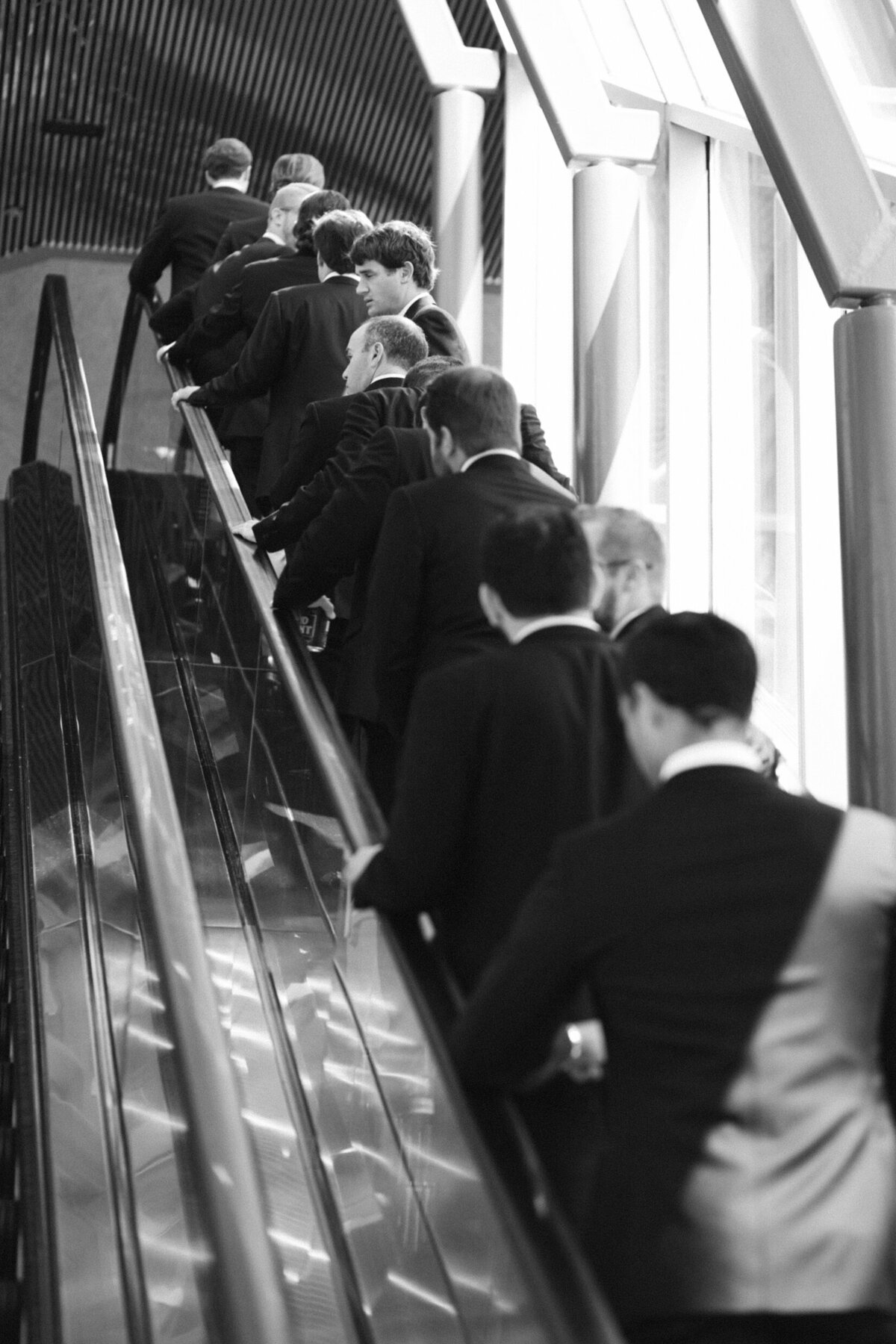 A black and white wedding photo of the groom and grooms men going up an escalator to the wedding reception