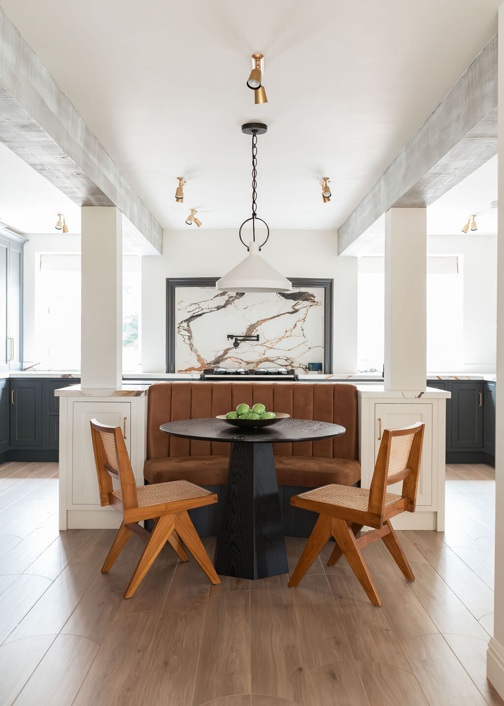 Modern kitchen with black cabinets, light wooden floor, and a central island. The kitchen has a built-in seating area with two wooden chairs and a small table.