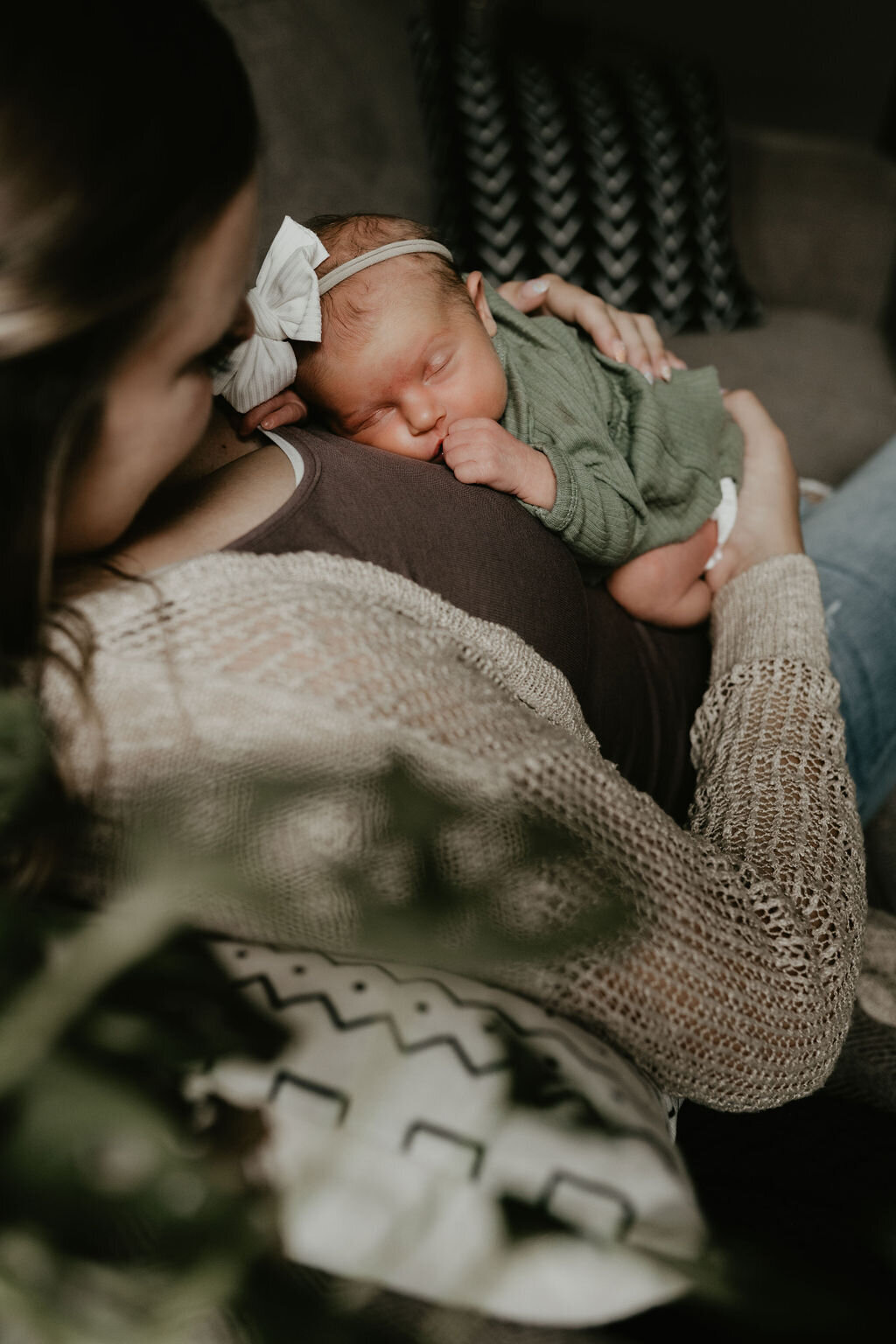 mom on couch holding new baby in a onesie and bow