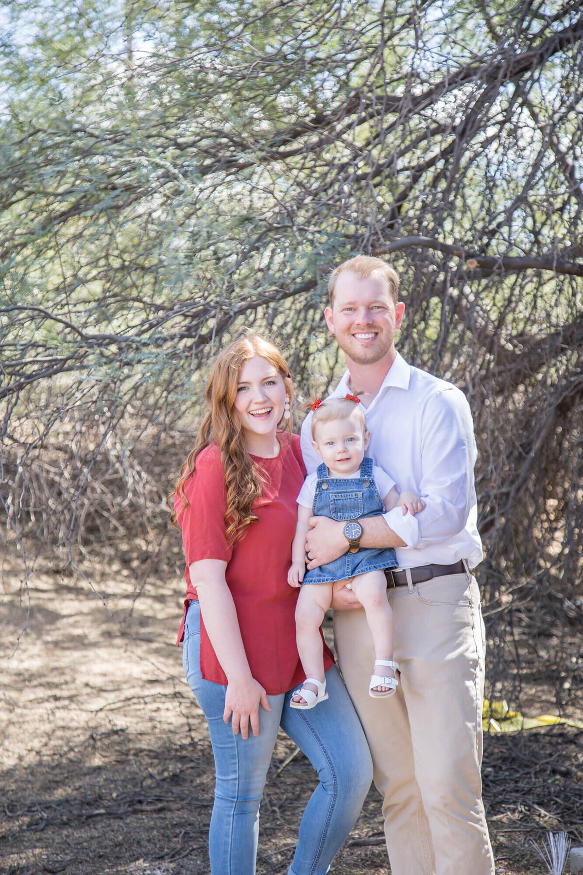 redheaded woman with husband in a white shirt and toddler girl in denim dress and pigtails