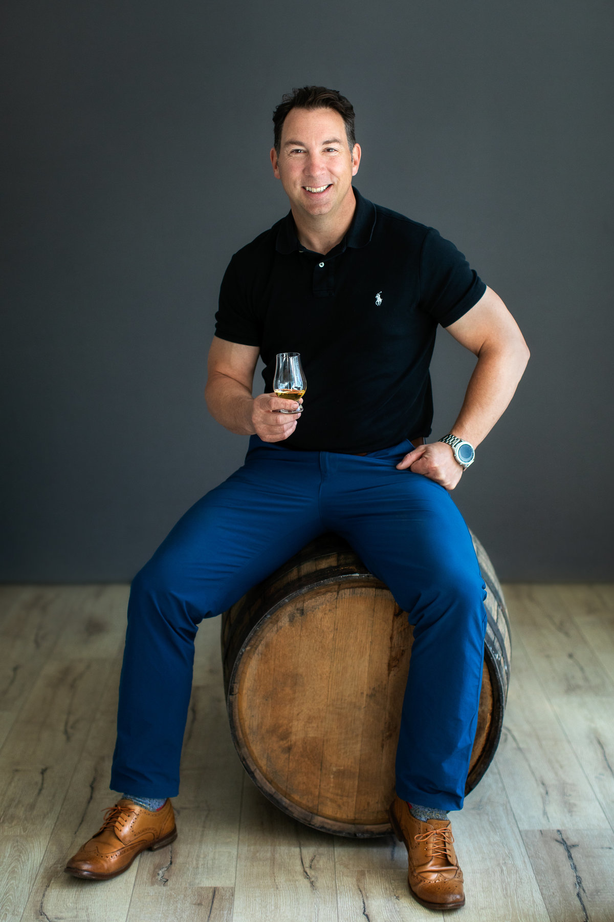 Portrait of man sitting on a whiskey barrel holding a glass