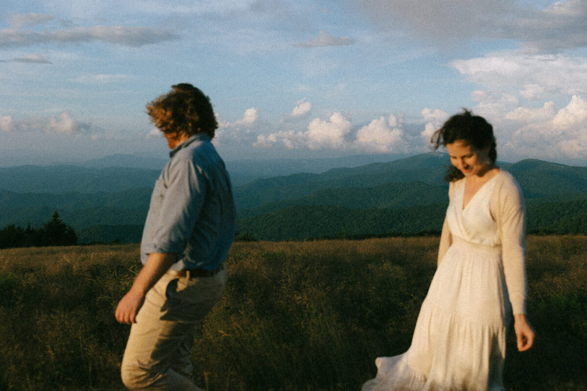 Couple walking through tall grass while watching the sunset over Roan Mountain outside of Asheville NC, photographed by Andrea-Marie Photography