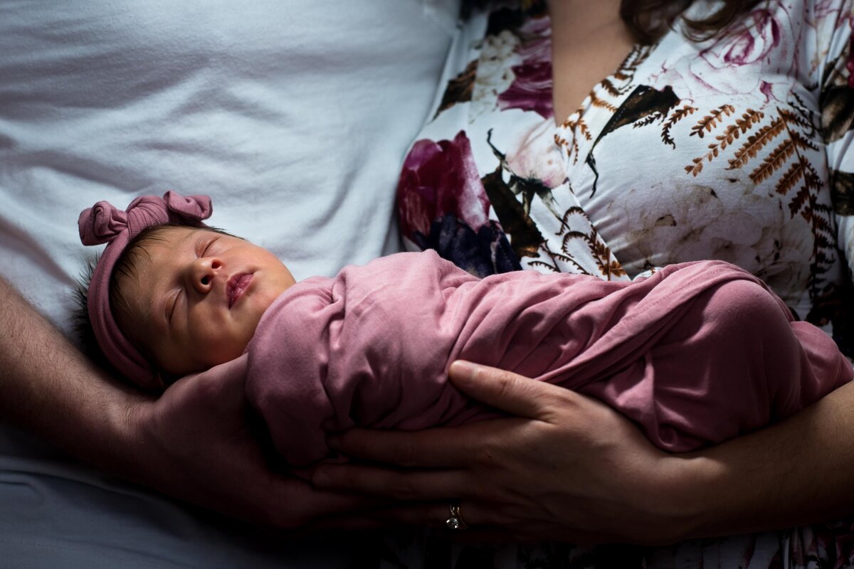 a newborn wrapped in a pink blanket is held by her parents