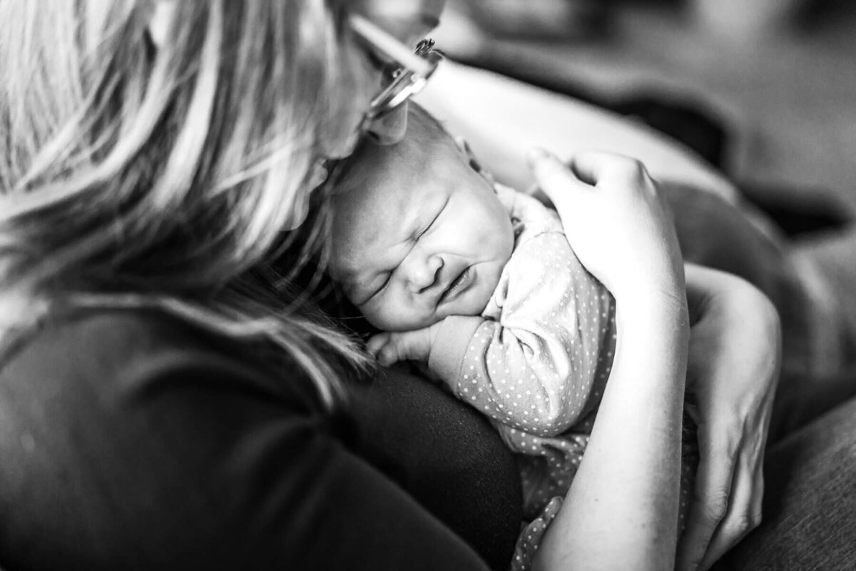 A black and white image of a mom hugging her newborn to her chest during an in home photo session.