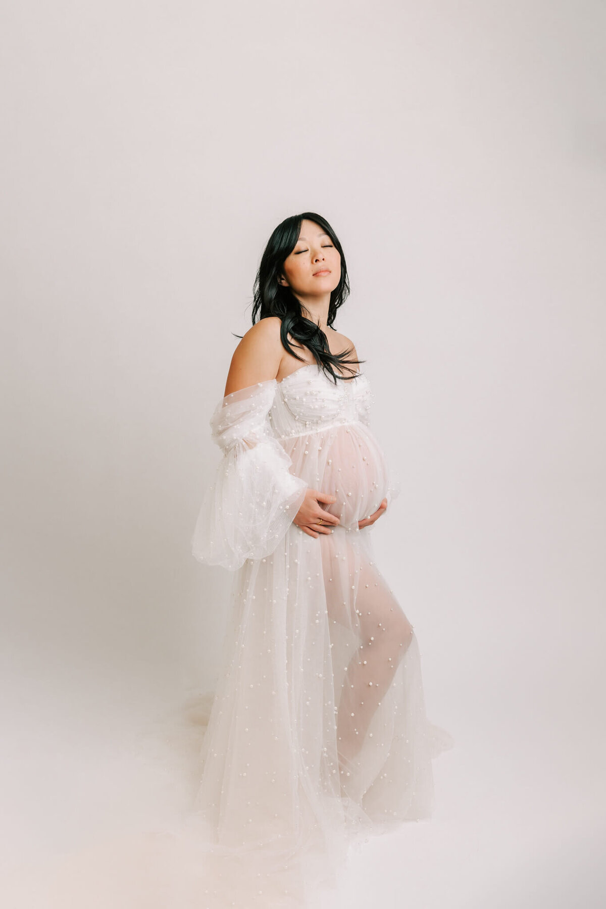 portland mom holding belly in her fine art maternity portrait session  Her eyes are closed and she is holding her belly.