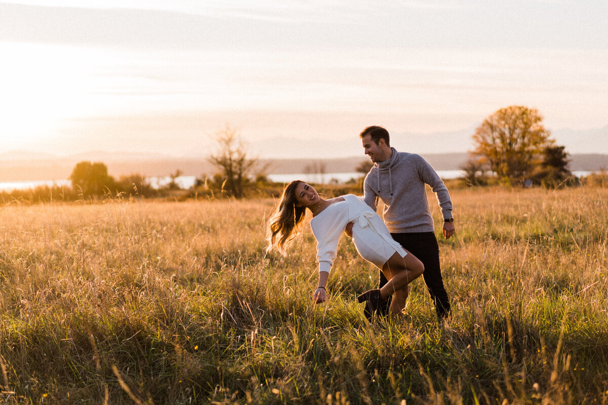 Couple dancing and hugging in large meadow at sunset in Discovery Park, best spot for engagement photos in Seattle