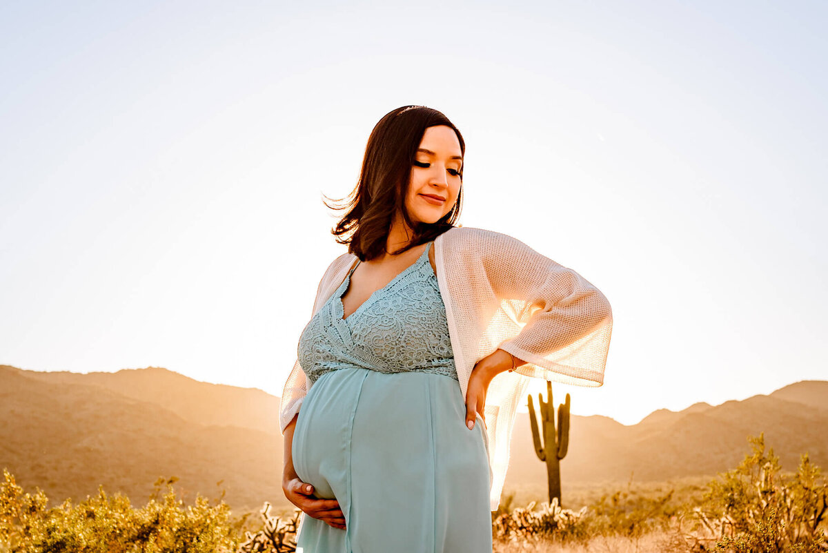 maternity mom in blue gown holding her hand and back during portrait session with Amber of Cactus & Pine Photography LLC in Arizona