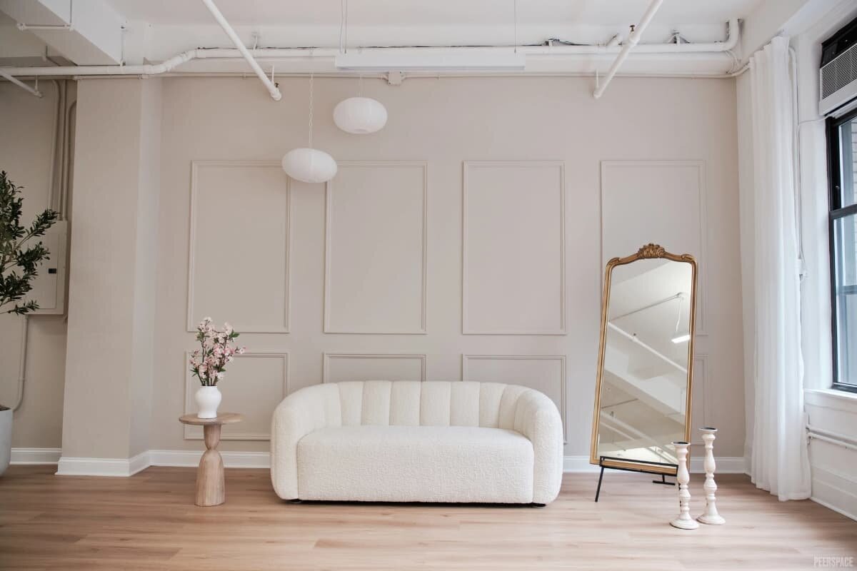 Minimalist NYC photography studio with cream sofa, full-length gold mirror, and soft natural light.