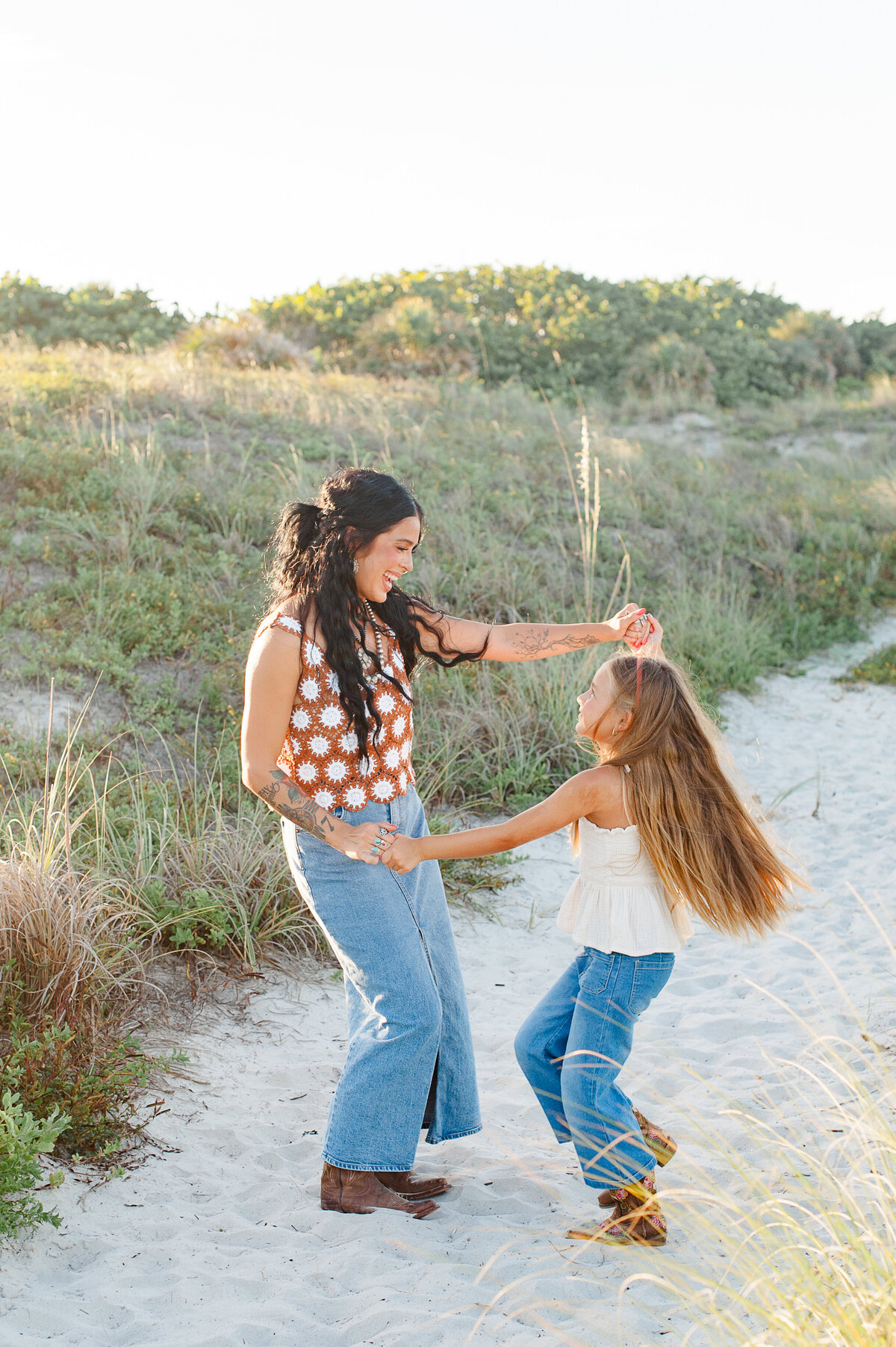 Young daughter dancing with her mother on the beach near the dunes at sunset