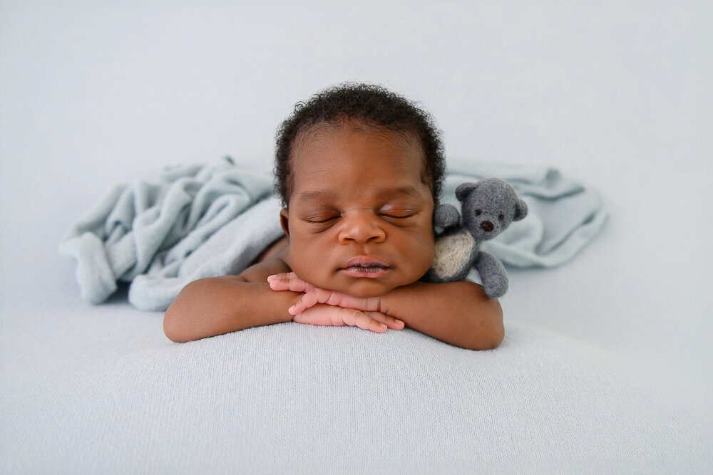 newborn baby boy on a blue background holding a tiny bear.