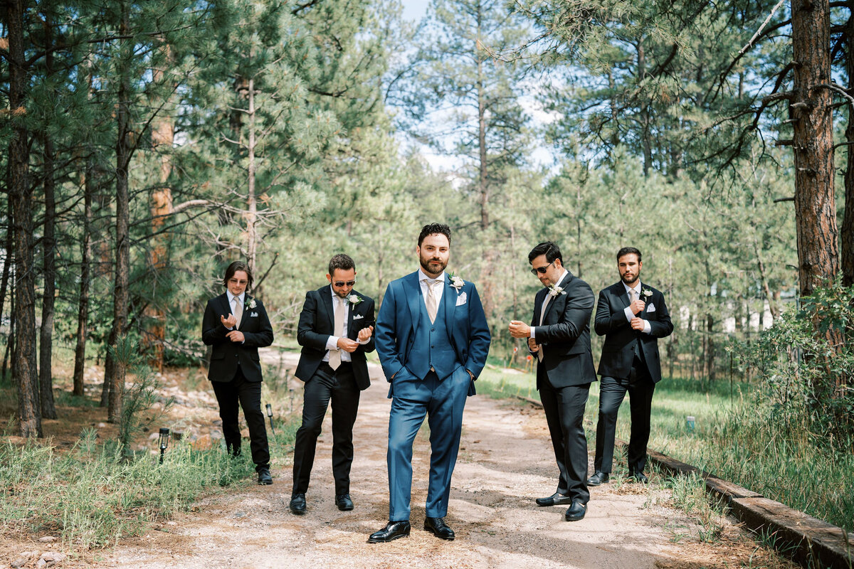 groomsmen adjust outfits while groom looks at camera