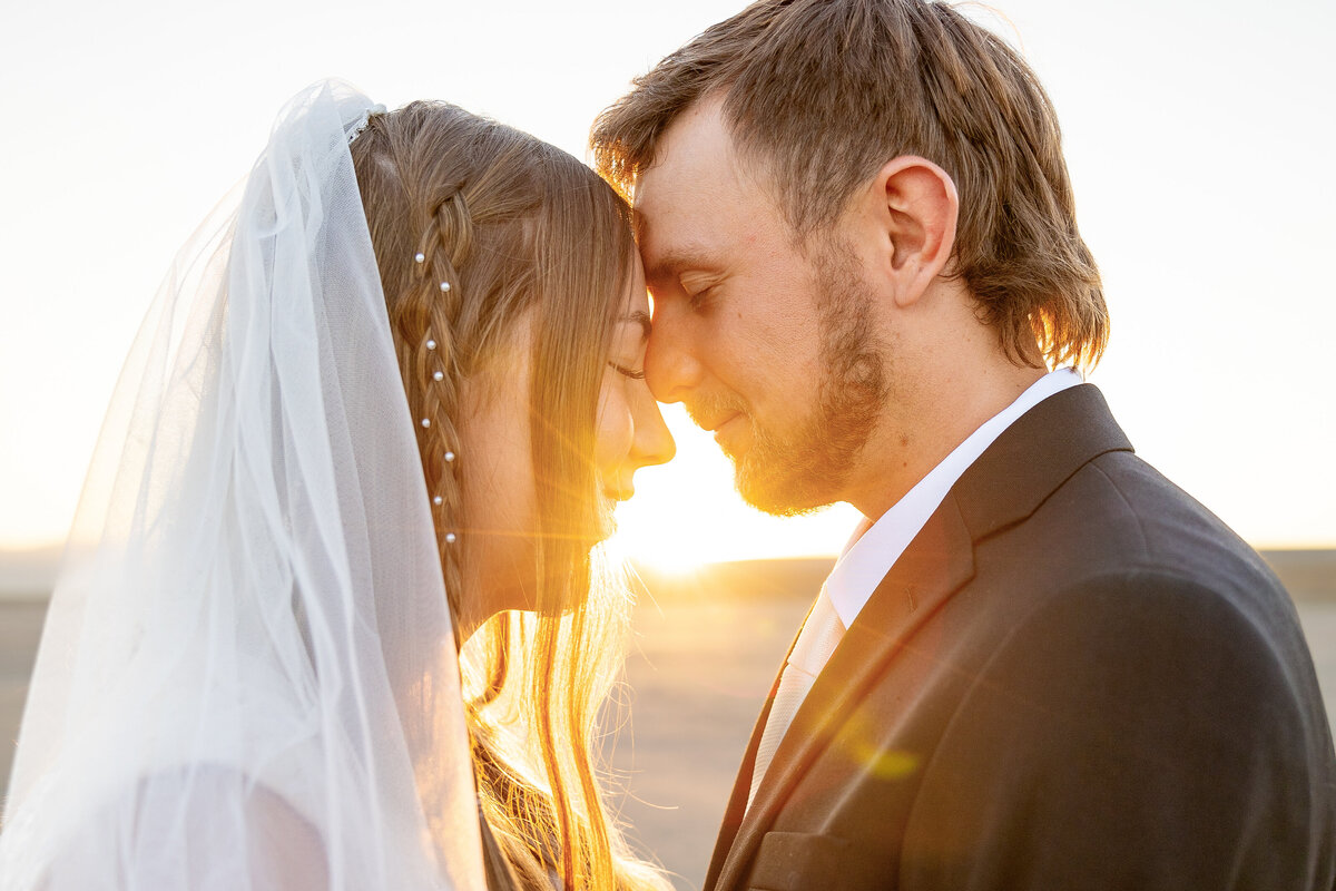Bride and groom touching foreheads with the sun rising behind them, creating a golden glow.