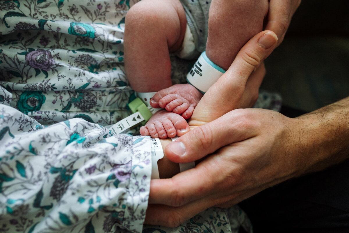 newborn feet with hospital bracelets held in parents hands
