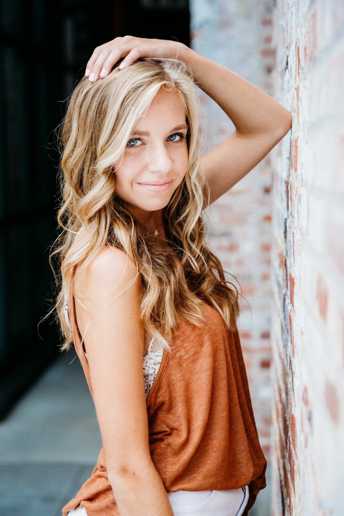 Graduate standing with her elbow propped up on a wall looking at the camera during her senior portrait session.