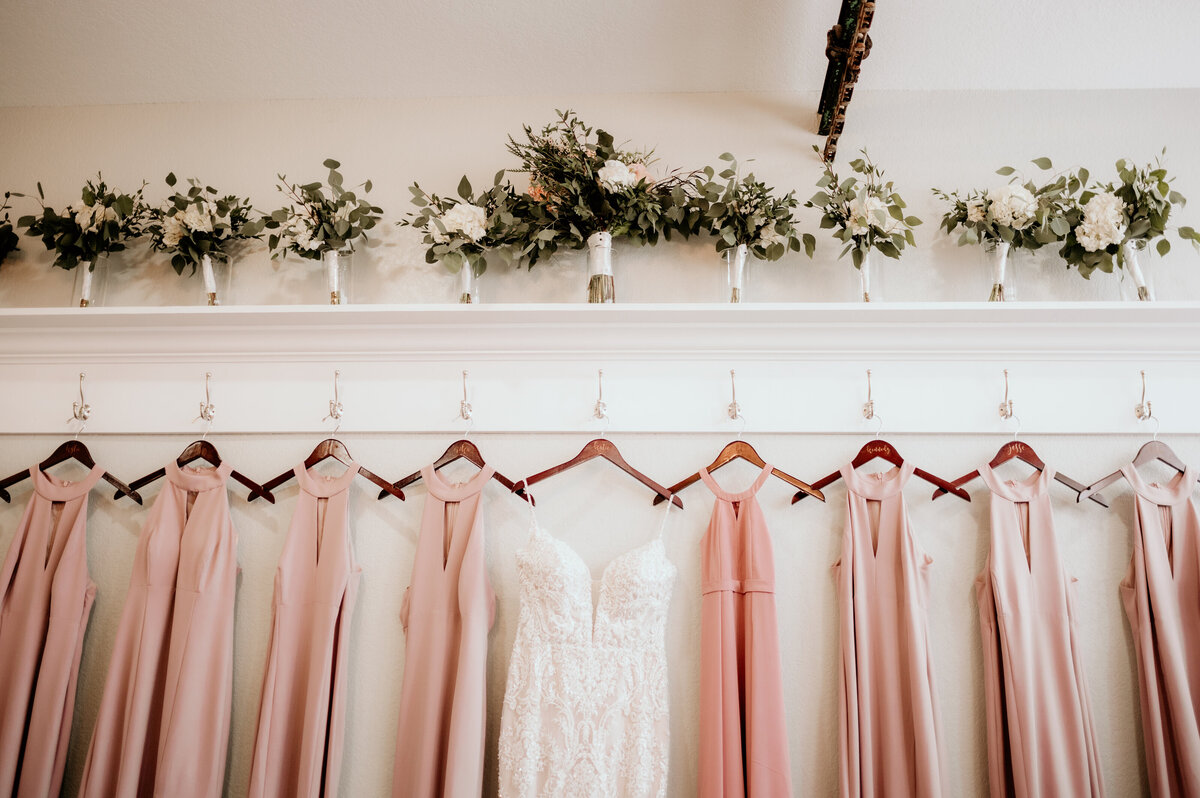 lace wedding dress and pink bridesmaids dresses hanging together at wedding venue in the bridal suite