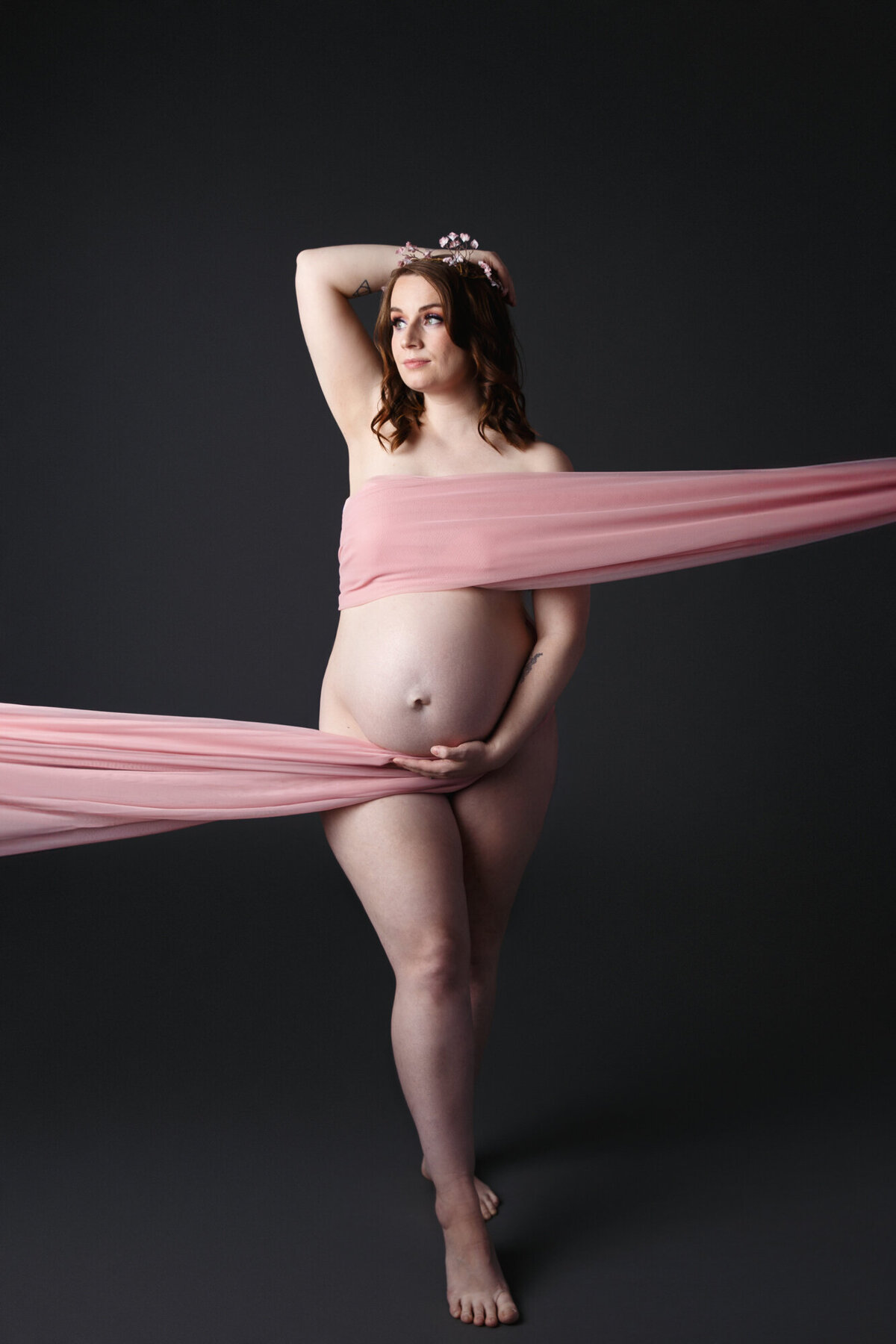Maternity photo taken in studio of a pregnant woman wrapped in a pink scarf on a dark gray background