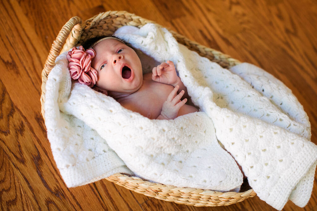 A newborn is caught mid yawn, wrapped in a blanket in a basket.