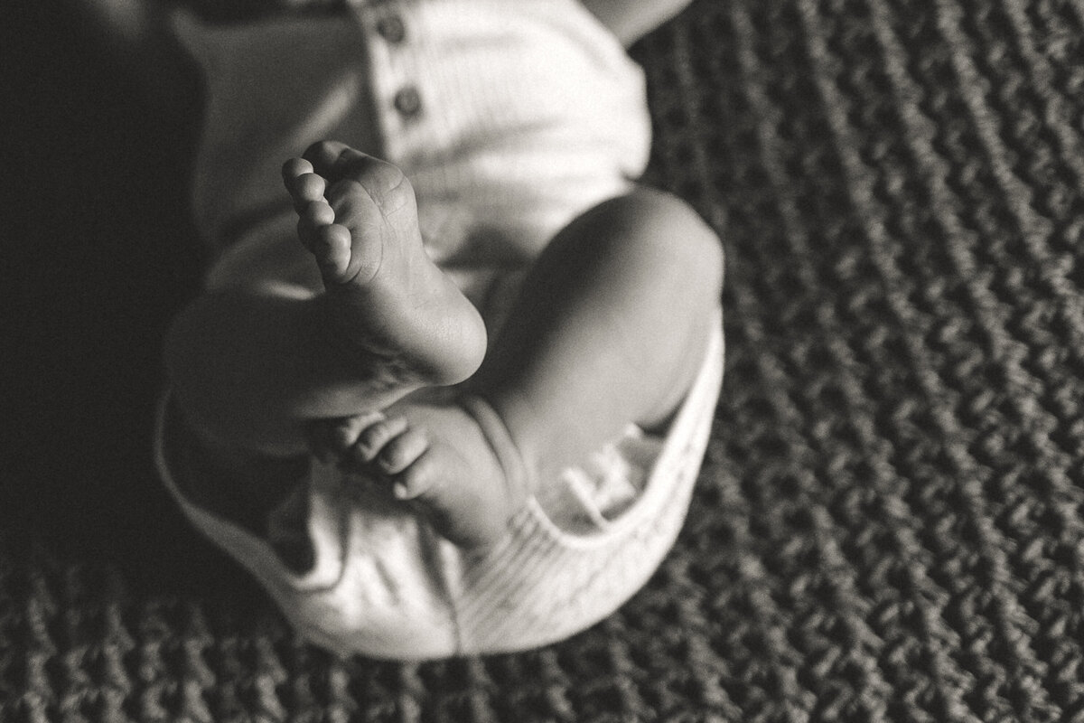 black and white image of crossed newborn baby feet in home lifestyle session in longmont colorado with alexis adkins photography