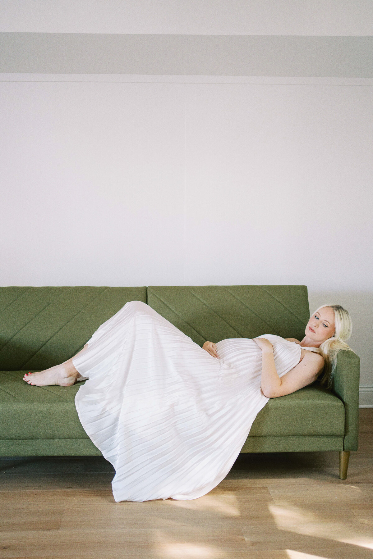 mom laying on the couch holding belly during maternity photos