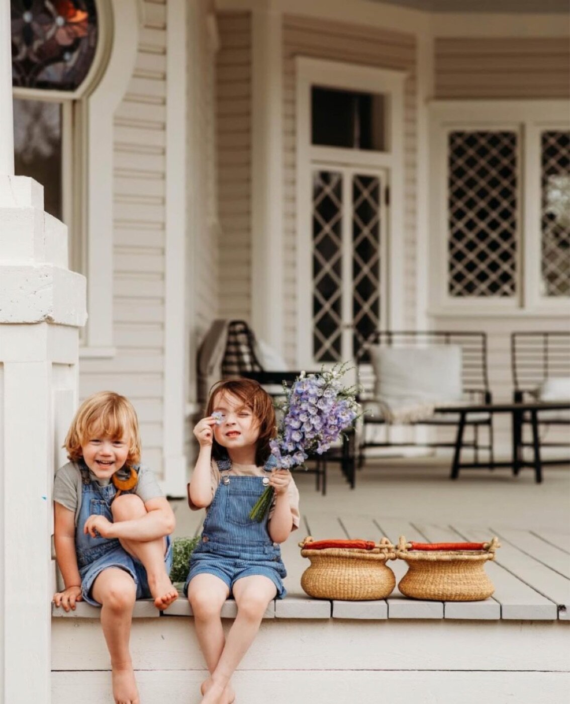 Two young kids in overalls laughing on the mansion's front porch steps