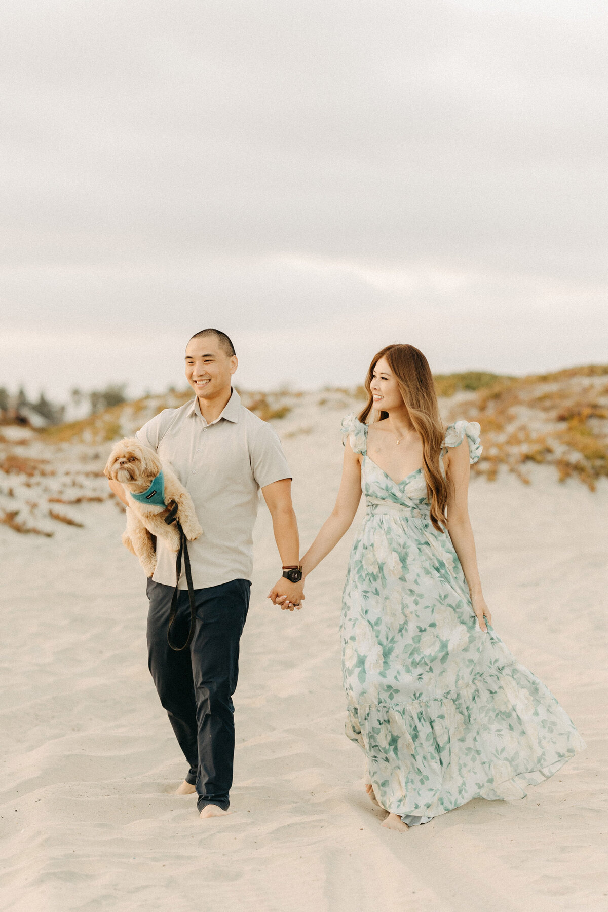 Couple strolling barefoot along Coronado Beach, the man carrying their small dog.