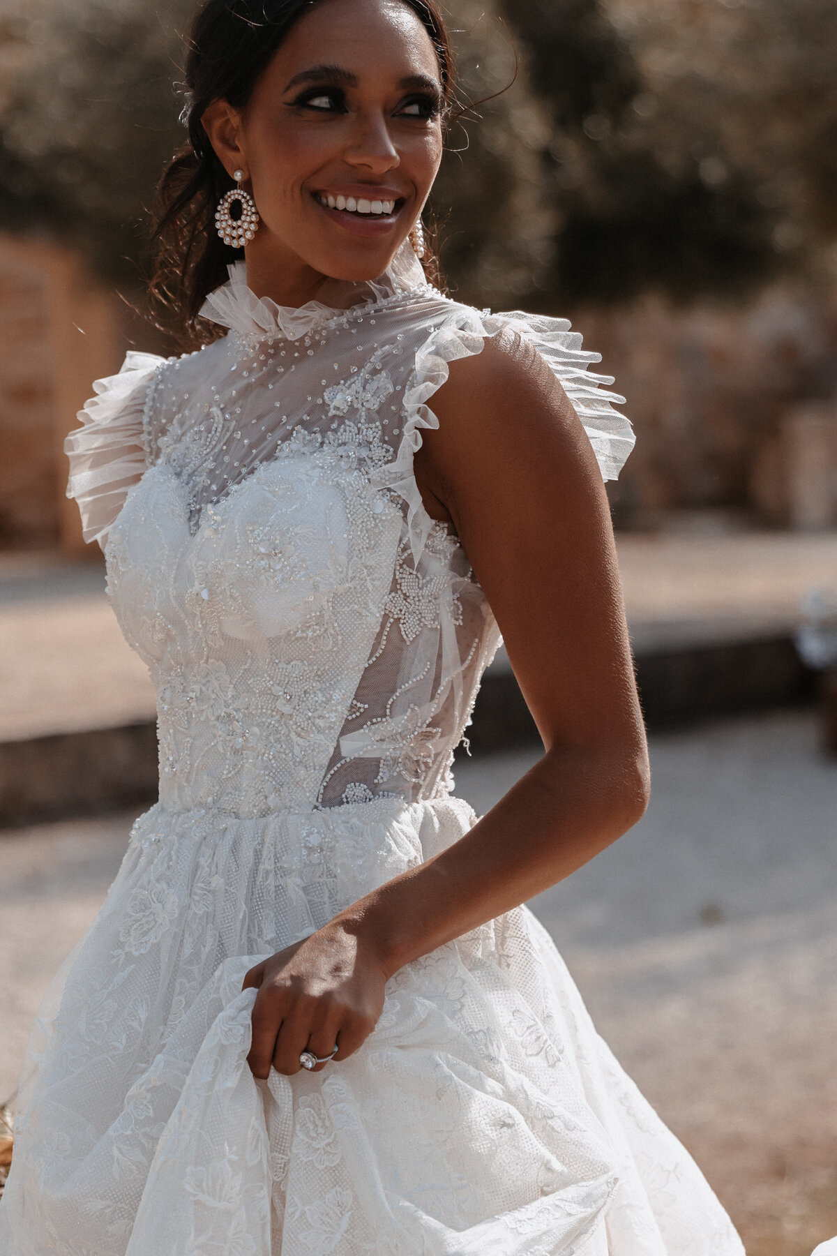 Smiling bride in a lace wedding gown with ruffled sleeves and intricate beading at Sunstone Winery.