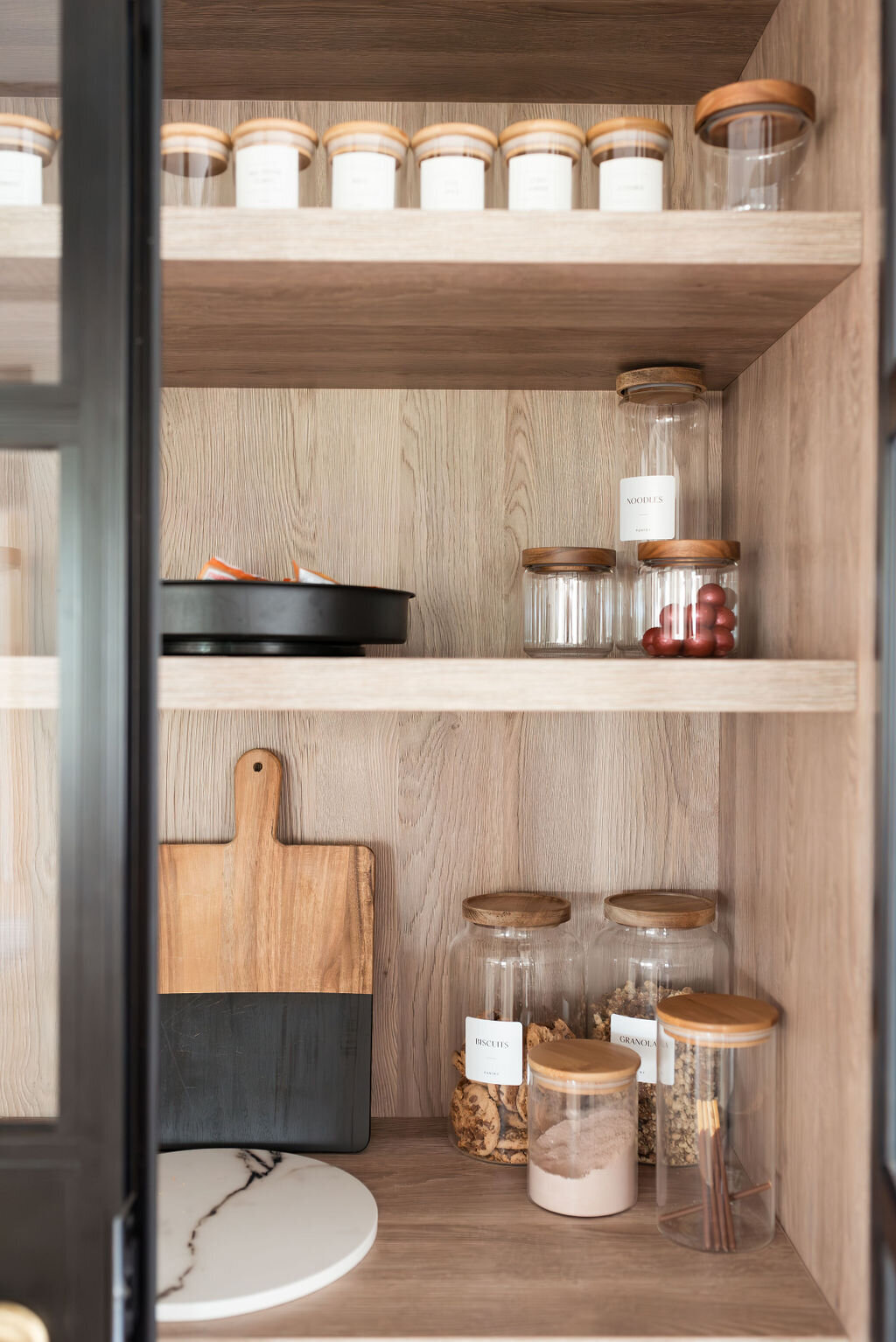 Built-in pantry cabinet with glass doors with black frames. Inside the open doors are spices organized in glass jars.