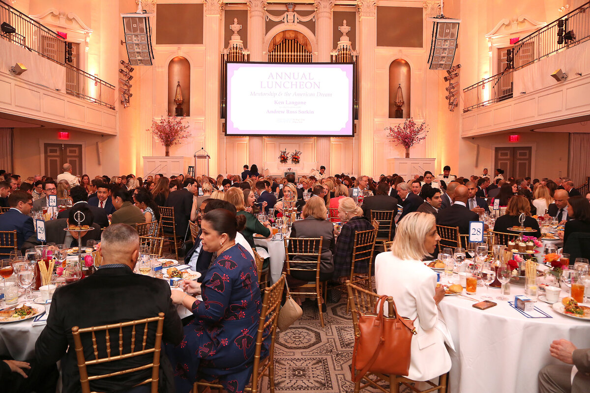 Wide view of the ballroom set with round tables and guests listening to the program.