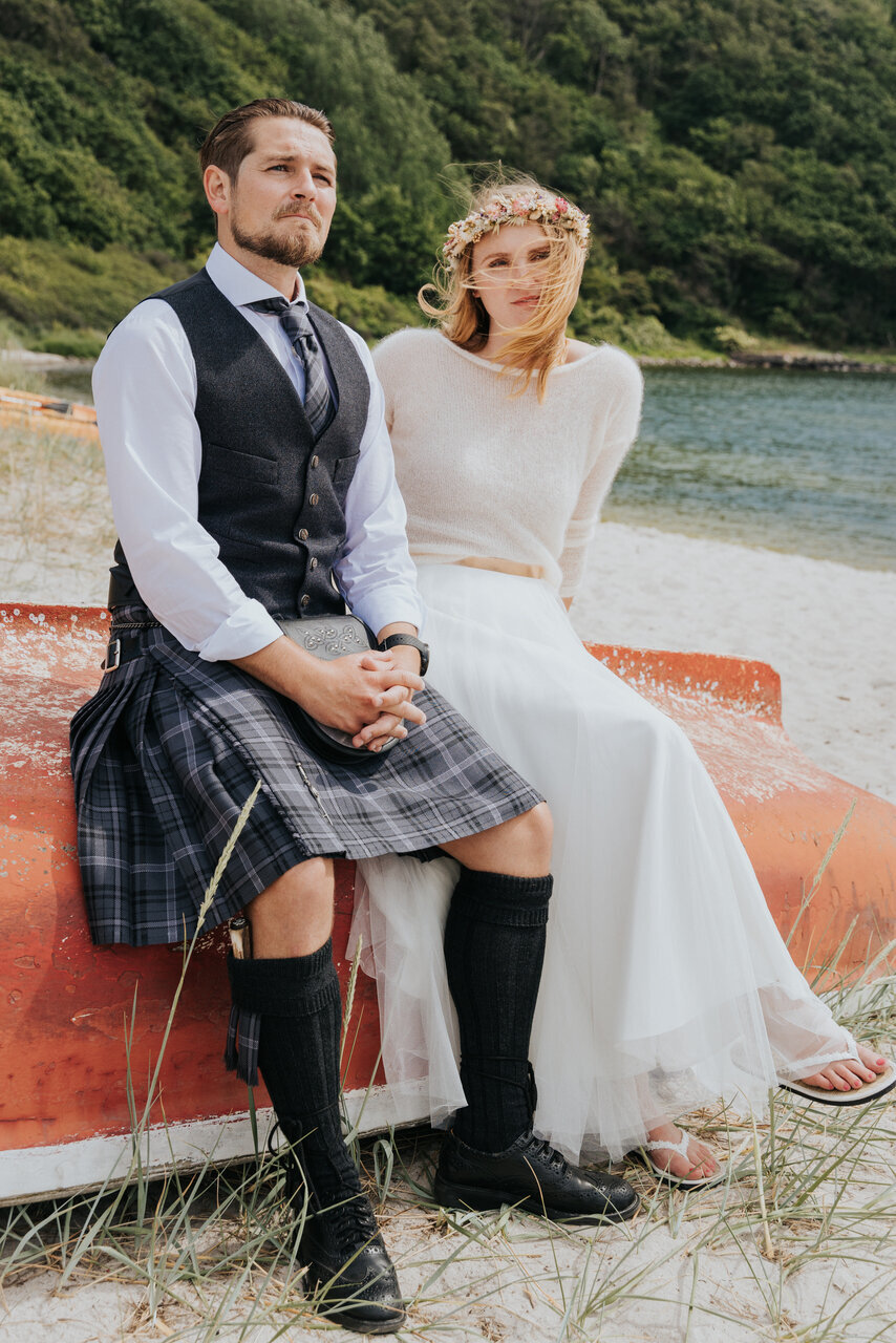 A bride and groom sitting on a boat in one of Bornholm’s  beaches, enjoying the beautiful shore  during their adventure elopement