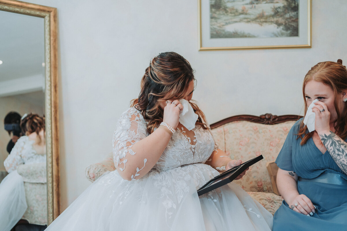 A touching candid moment as a bride in her lace wedding gown and her bridesmaid shed tears of joy, sharing a deeply emotional experience on the wedding day in Virginia.