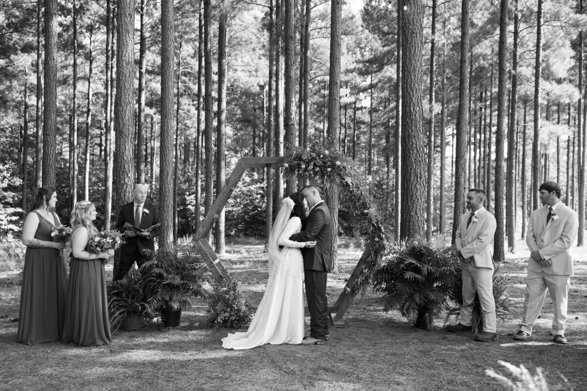 A newlywed couple during their first kiss with their wedding parties on either side