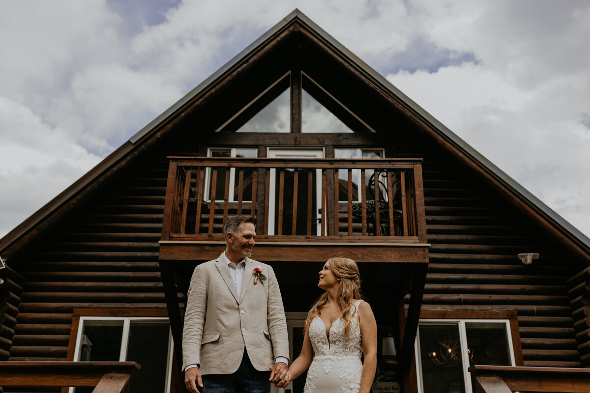 bride and groom standing together in front of a cabin looking at each other