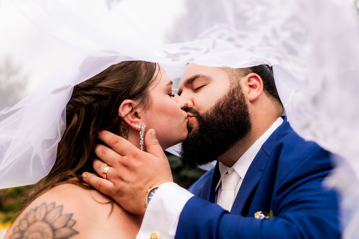 A bride and groom kiss under a veil.