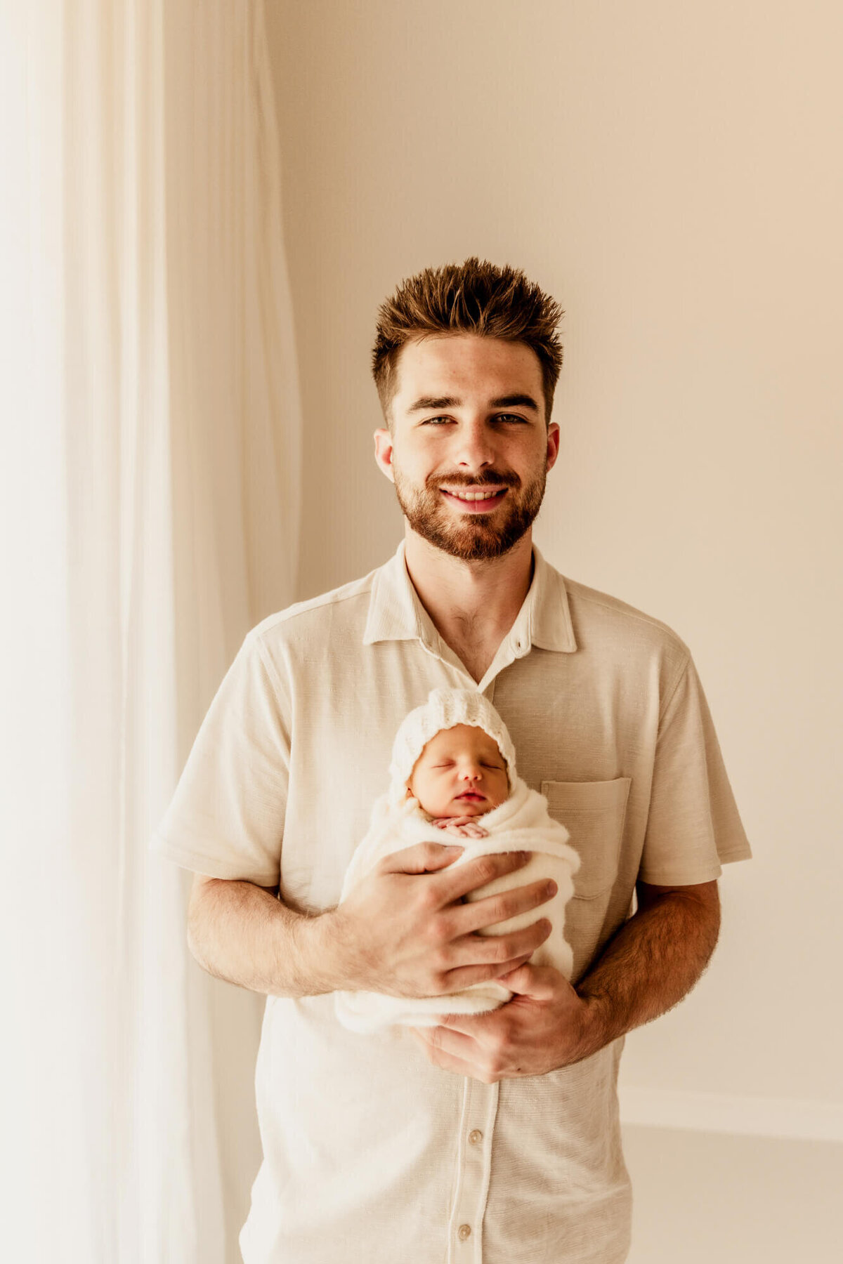 Father holding is newborn daughter in his arms smiling.