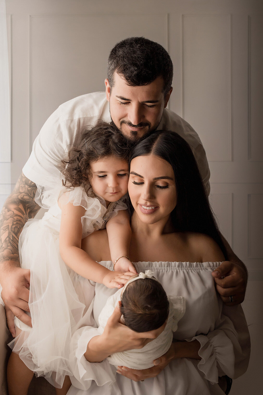 Lovely family of 4 holding their new baby with dads arms wrapped around his family