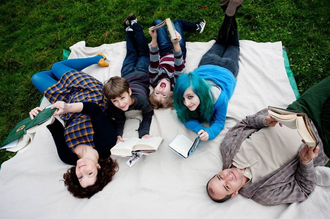 Colorful family laying together on a blanket in the park, mom , dad, daughter and 2 sons laying together reading books,