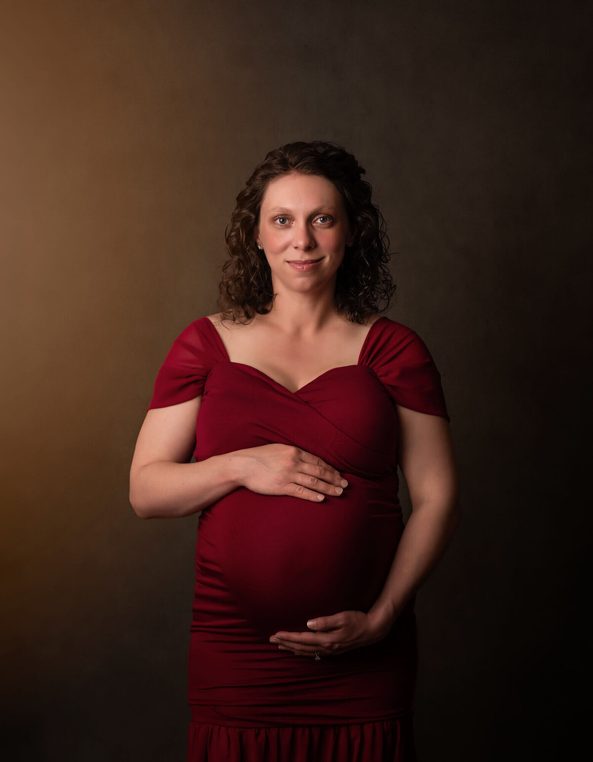 A beautiful mama to be cradles her bump and smiles for the camera during her portrait session with an Asheville Maternity Photographer