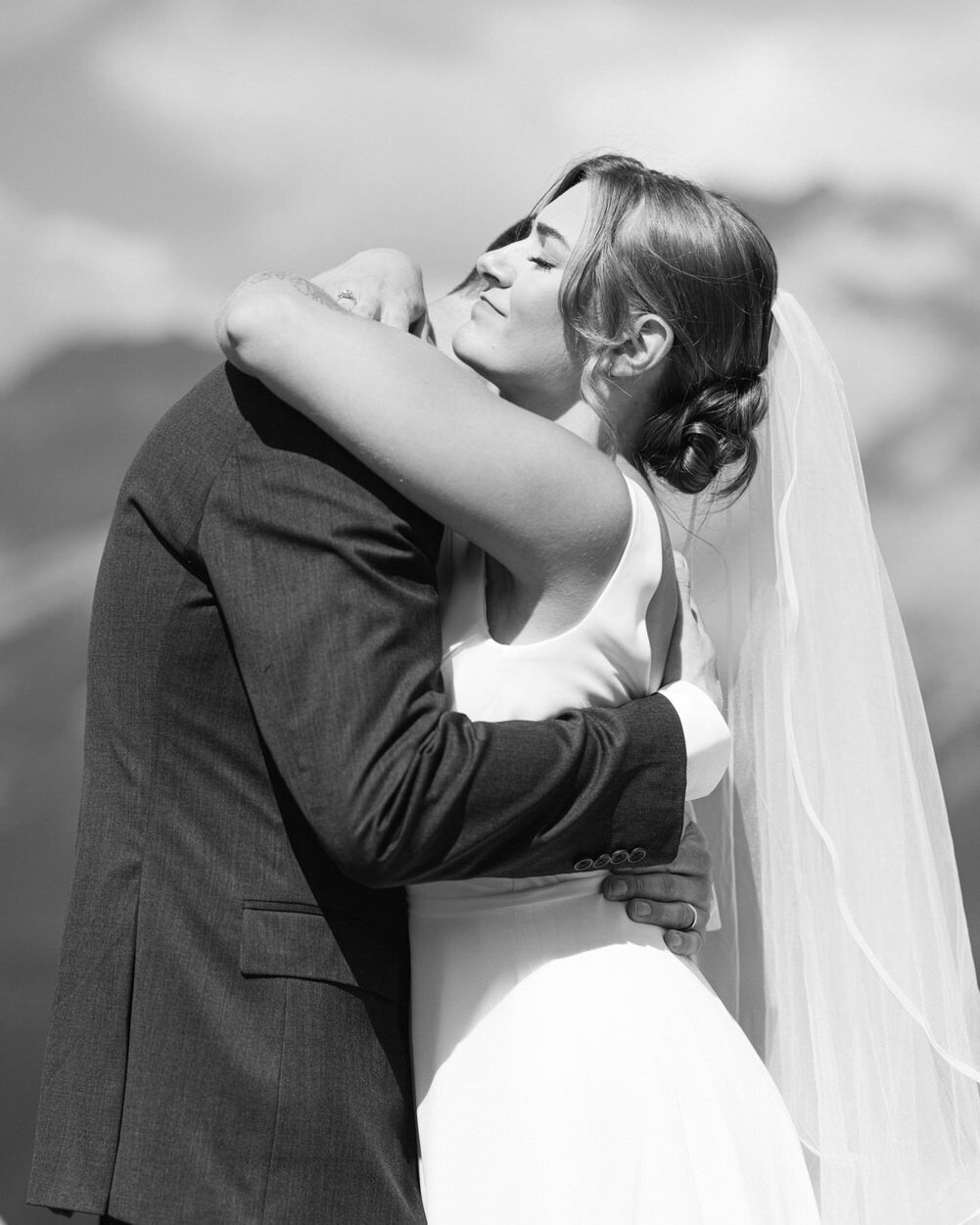 This heartfelt photograph captures an intimate moment as the groom hugs his bride after their wedding in Banff National Park. The natural beauty of the park enhances the warmth and love shared between the couple on their special day.