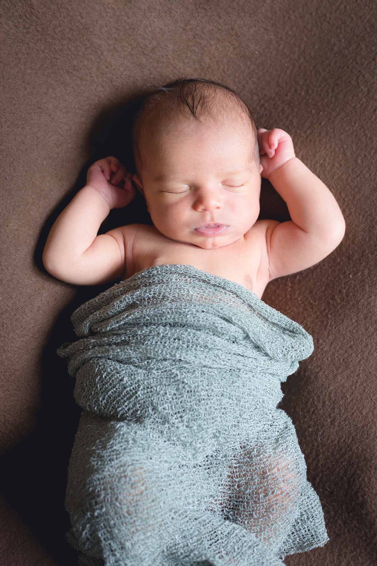 Newborn asleep with arms near his head on a brown blanket in Columbia SC